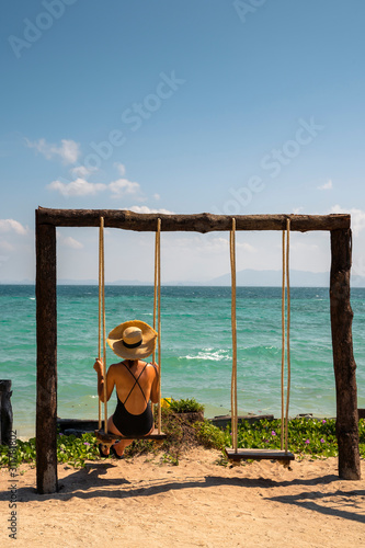 Travel to Thailand concept. Woman on her romantic honeymoon getaway isolated on a paradisiacal beach with palm trees. Expensive luxury resort for married couples and single people. Relax on a swing.