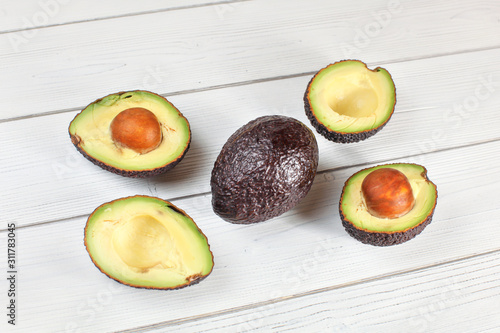 Avocado halves, and one whole fruit arranged on white boards desk photo