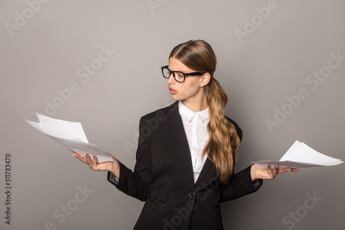 businesswoman in glasses and suit holding sheets of paper isolated on grey