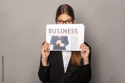 businesswoman holding business newspaper in front of face isolated on grey