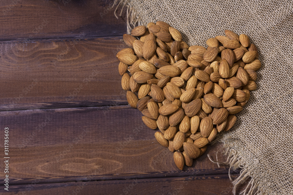 Raw almonds in heart shape. Burlap sack old wood table Raw almonds in heart shape. Burlap sack old wood table