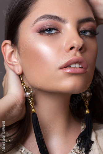 Close up portrait of a beautiful girl with professional makeup, ideal skin, rose eyeshadows and lips and long earrings