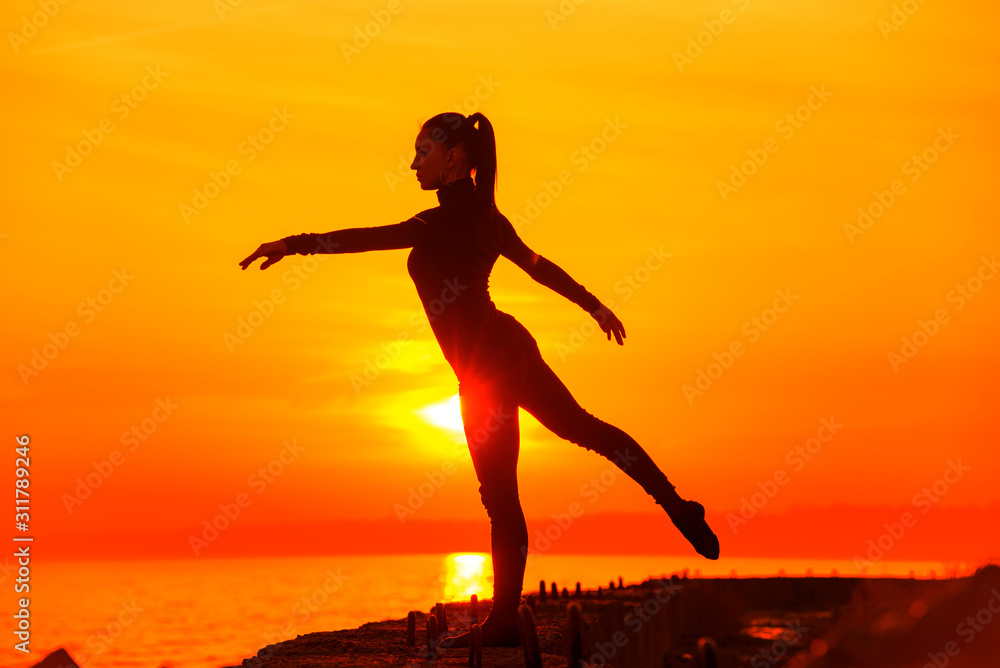 Silhouette of woman doing yoga meditation during sunset with natural golden sunlight on sea.