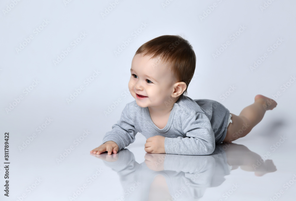 Little baby boy toddler in grey casual jumpsuit and barefoot lying on floor, smiling and looking up Little baby boy toddler in grey casual jumpsuit and barefoot lying on floor, smiling and looking up