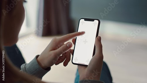 Over shoulder shot of caucasian girl using smartphone with vertical green white screen. Woman tap on display, scrolling, wathing content. Close up, slow-motion. photo