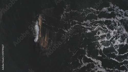 A small wave washing over a barely submerged rock at sunrise AERIAL TOP DOWN photo