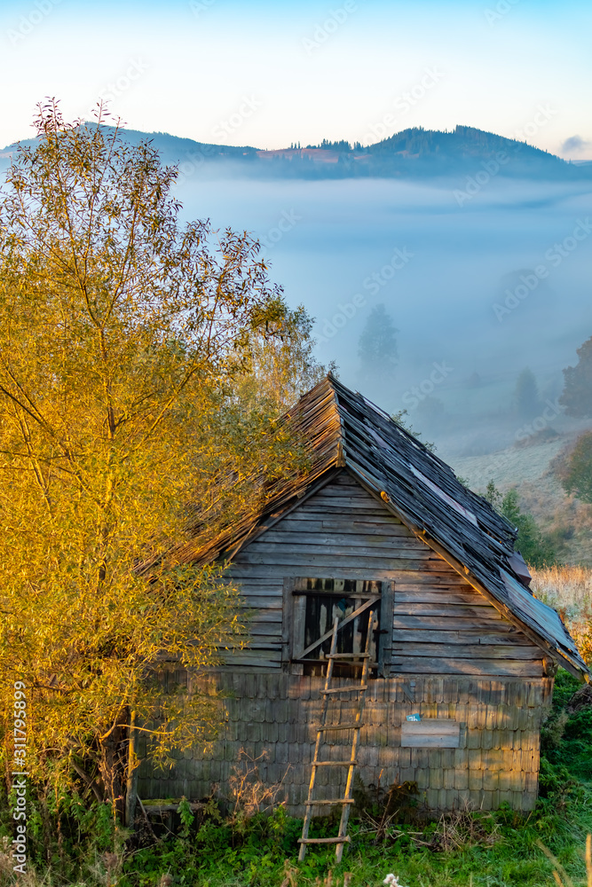 Beautiful autumn landscape during sunrise with old hut and fog in valley with mountains, Romania Beautiful autumn landscape during sunrise with old hut and fog in valley with mountains, Romania