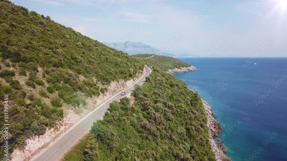 Aerial shot of a car following the beautiful coastline of Montenegro Aerial shot of a car following the beautiful coastline of Montenegro