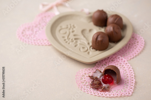 Chocolate Covered Cherries displayed in a heart shaped cookie mold. One isolated in front on pink heart-shaped doilies. Beige background with room for text.