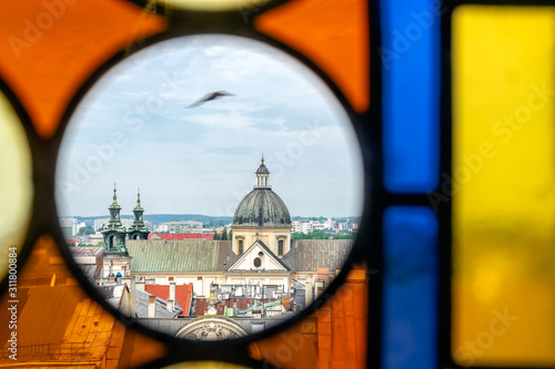 Upper part of St. Anne's Church - dome, towers and roof - in Krakow, Poland. View from the Town Hall Tower through window with colored stained glass windows. A bird flies in the sky.