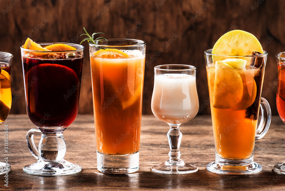 Selection of autumn or winter seasonal alcoholic hot cocktails - mulled wine, glogg, grog, eggnog, warm ginger ale, hot buttered rum, punch, mulled apple cider on wood background, copy s