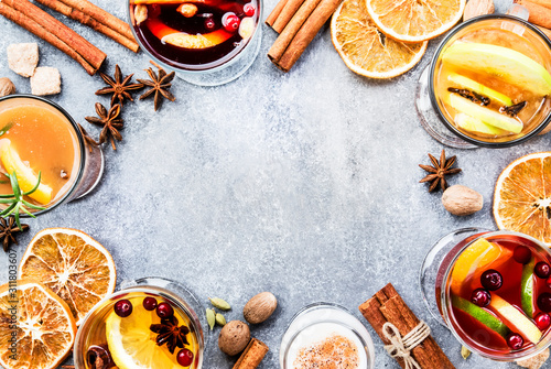 Various autumn or winter seasonal alcohol hot cocktails - mulled wine, glogg, grog, eggnog, warm ginger ale, hot buttered rum, punch, mulled apple cider on gray background, top view with copy space