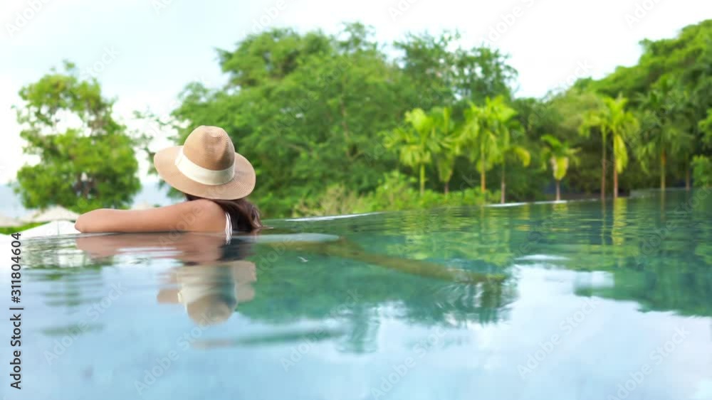A woman wearing a hat, relaxing in an infinity pool at a luxury hotel ...