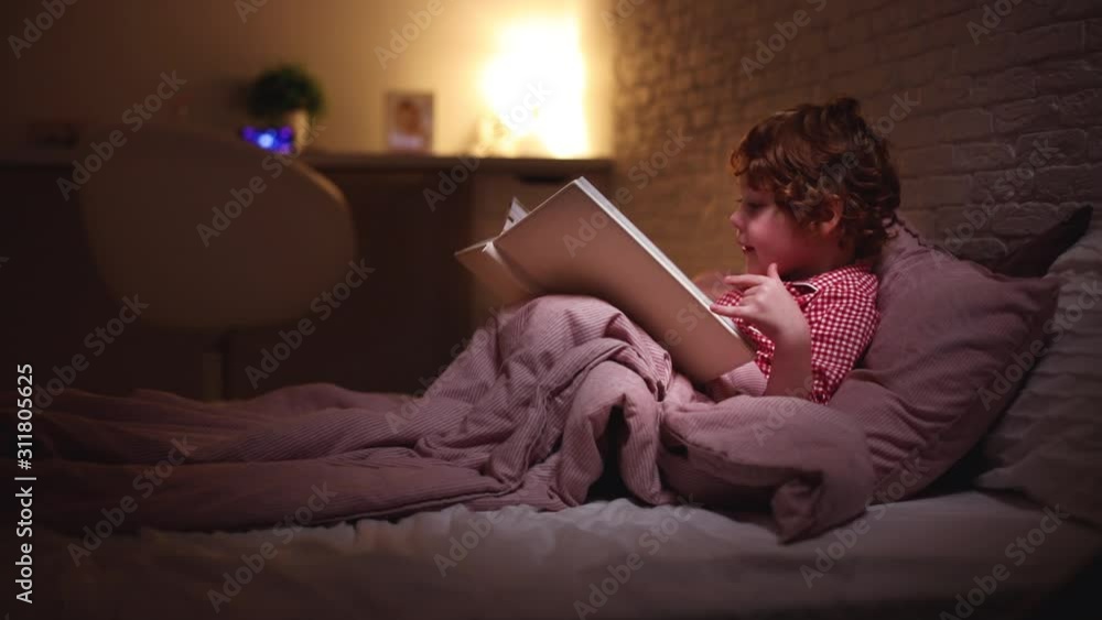 toddler baby boy reading the book in bed before going to sleep toddler baby boy reading the book in bed before going to sleep