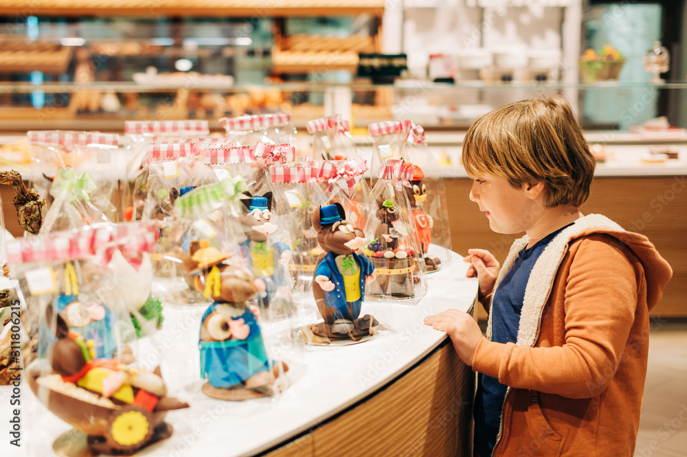 Funny kid boy admiring easter chocolate bunnies in chocolate shop