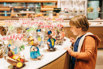 Funny kid boy admiring easter chocolate bunnies in chocolate shop