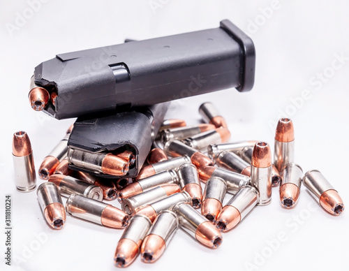 Multiple 9mm hollow point bullets with two loaded 9mm pistol magazines laying on top of them on a white background  photo