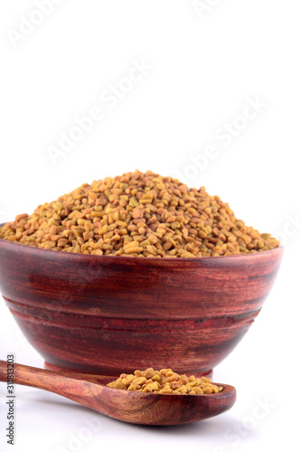 Fenugreek seeds in wooden bowl with spoon isolated on white background photo