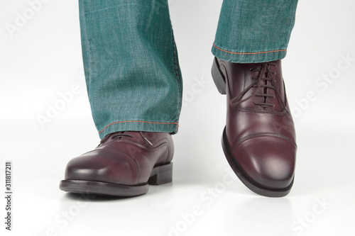 Male legs in jeans and brown classic shoes on white background