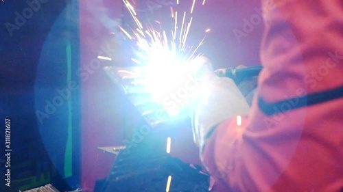Close-up welder technician wear protection bodysuit  and safety mask working with workpieces via welding machine until it sparks, industry 4.0