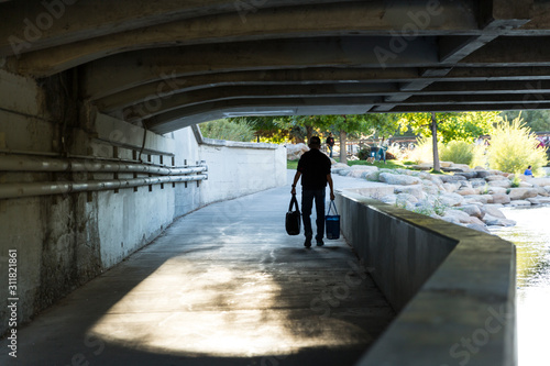 Person carrying bags on their way home from shopping under a bridge on the Truckee river