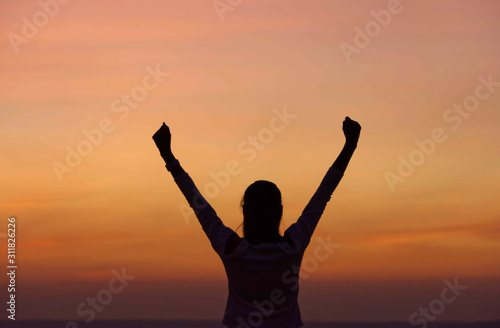 The black silhouette of behind the women raise their arms Background sky orange light of sunset.