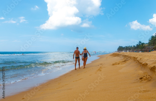Back view of young family with a little daughter walking along the beach together holding hands