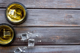 Whiskey near ice cubes on dark wooden background top-down frame copy space