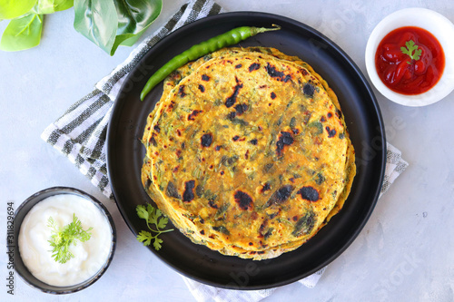 A Food called Methi paratha or Methi thepla is a Indian breakfast dish served with curd and ketchup. with copy space.