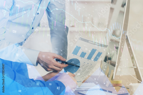 Double exposure of chart with businessman typing on computer in office on background. Concept of hard work.