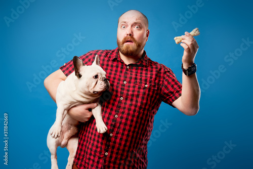 Surprised man in shirt holds bulldog and bone on empty blue background