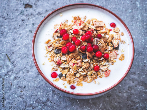 Bowl with yoghurt, muesli granola and lingonberries on gray rough stone texture background. Healthy lifestyle breakfast