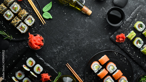 Set of sushi rolls with ginger, wasabi and soy sauce on a black stone background. Japanese Traditional Cuisine. Top view. Rustic style.