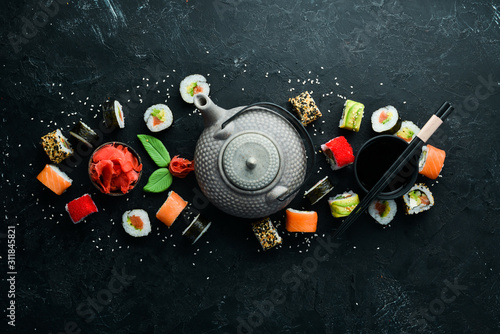 Background of sushi rolls with tea, ginger, wasabi and soy sauce on a black stone background. Japanese Traditional Cuisine.