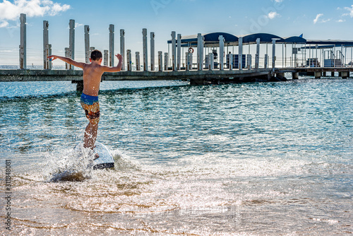 Young caucasian boy skim boarding on the ocean near a pier in Honolulu, Hawaii: joy and fun concepts