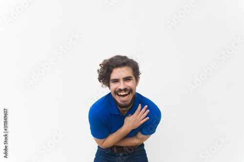 Happy excited guy laughing out loud, holding stomach. Handsome bearded young man in blue casual t-shirt posing isolated over white background. Joy or laughter concept