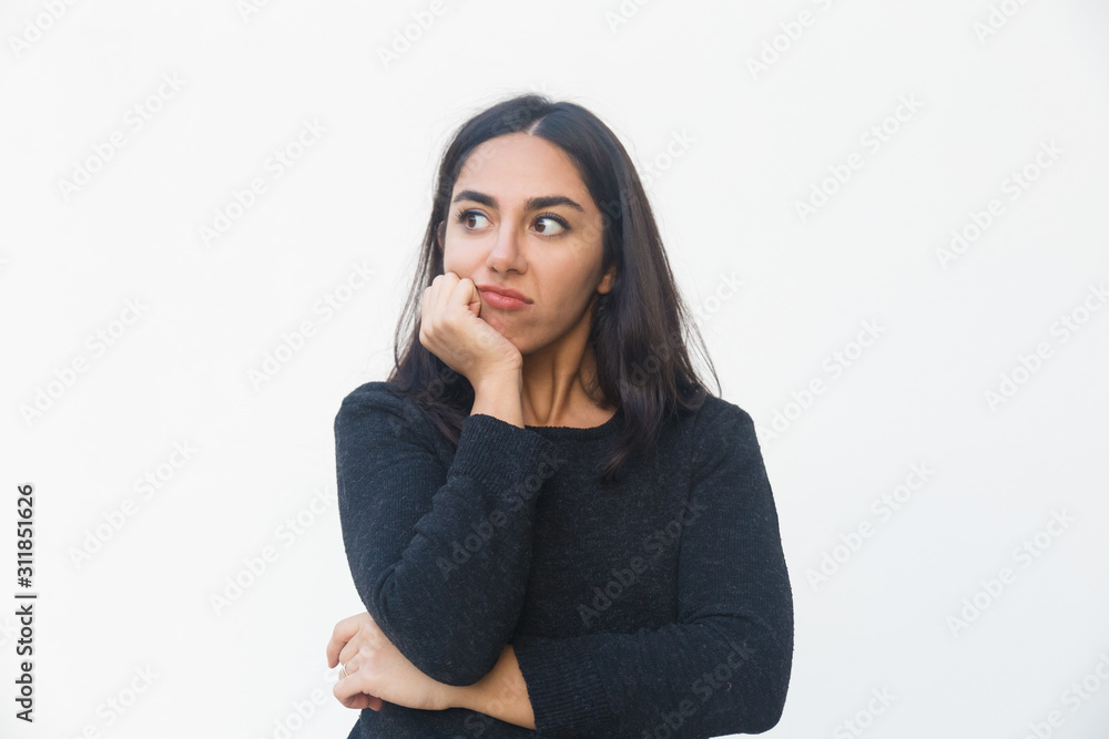 Pensive disappointed woman leaning chin on hand, looking away. Beautiful young woman in casual sweater posing isolated over white background. Thinking or advertising concept