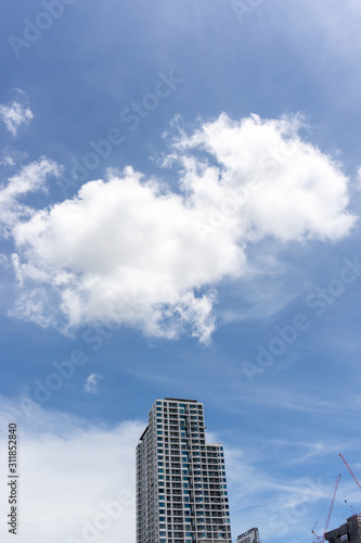 Beautiful white fluffy cloud formation on vivid blue sky in a sunny day above tower in big city, a part of Bangkok in Thailand