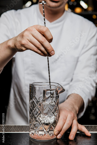 Bild auf Leinwand Bartender prepairing a cocktail at the bar stirring a drink in a mixing glass wi