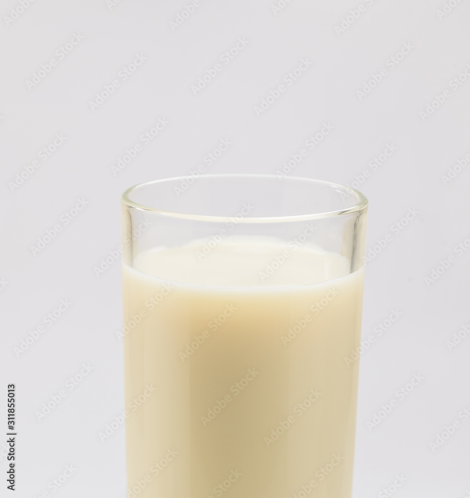 A cup of soy milk stands alone on a pale yellow background. A cup of soy milk stands alone on a pale yellow background.