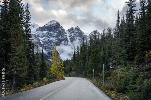 Driving on road in pine forest with rocky mountains at Moraine lake