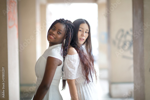 portrait of Asian and African american women in white dress against street