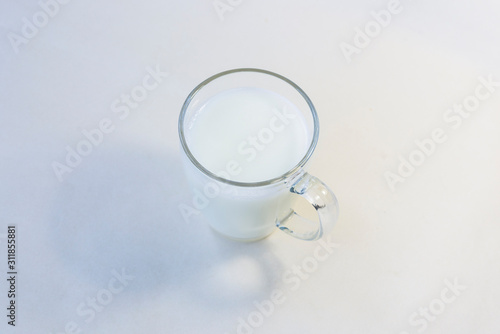 A cup of soy milk stands alone on a pale yellow background.