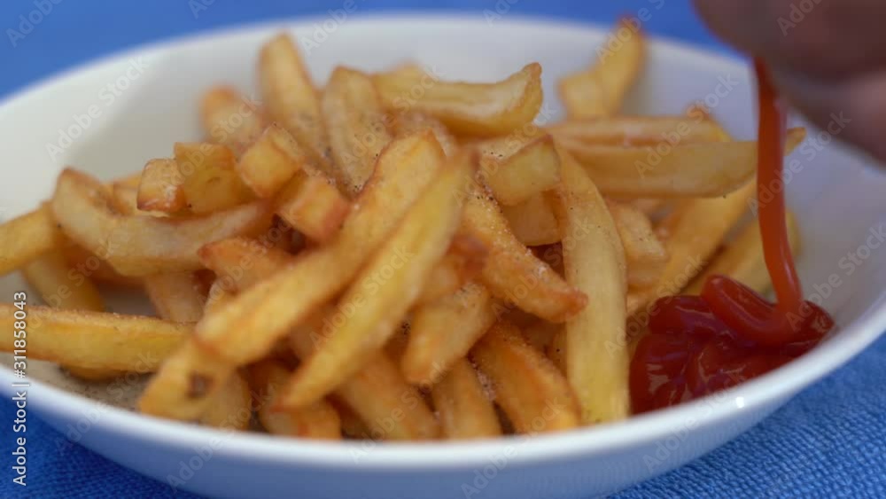 Closeup view of big white plate full of fresh hot tasty french fries. Woman adding tomato ketchup on plate and eating tasty salt fried potatoes. Real time 4k video footage. Closeup view of big white plate full of fresh hot tasty french fries. Woman adding tomato ketchup on plate and eating tasty salt fried potatoes. Real time 4k video footage.