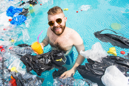 Problem of trash  plastic recycling  pollution and environmental concept - silly man swim and have fun in a polluted pool. Bottles and plastic bags float near them