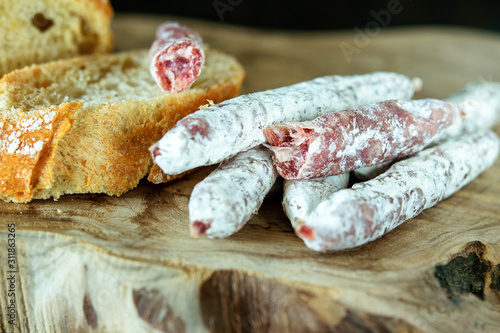 Thin spanish fingers of sausage fuet and white bread on the wooden natural board closeup. Healthy food concept. photo