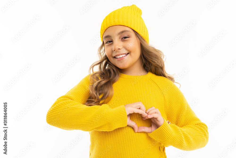 Little girl with in yellow hoody and hat shows a heart from her hands and smiles, portrait isolated on white background Little girl with in yellow hoody and hat shows a heart from her hands and smiles, portrait isolated on white background