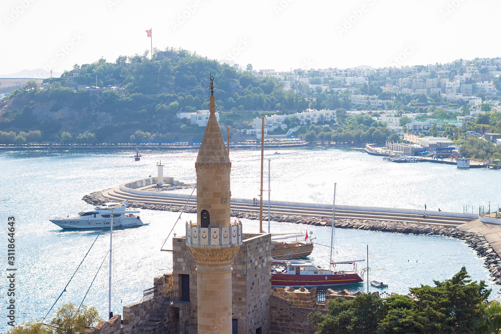 Fototapeta premium View of the Bodrum Castle Mosque's (Kale Camii) minaret (also known as St Peter Castle) and panoramic view on white buildings and Aegean sea on background Mugla, Turkey.