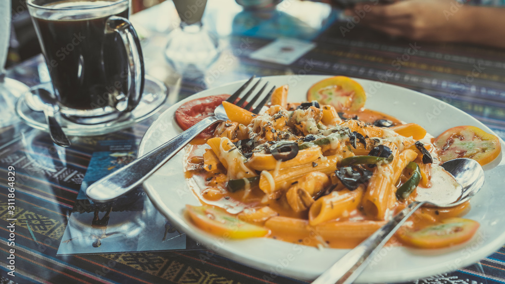 Delicious pasta with tomato sauce. Silverware placed on plate of palatable pasta with tomato sauce and olives on ornamental table in cafeteria