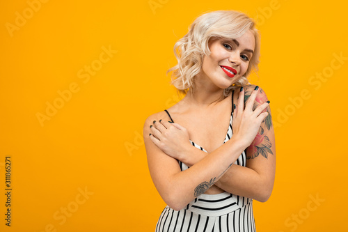 Beautiful young woman with short blonde curly hair and bright makeup folded hands and smiles, portrait isolated on orange background